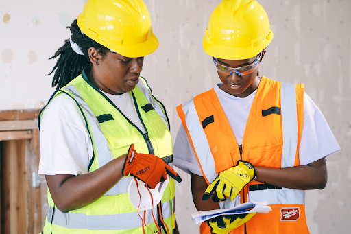 Two construction workers wearing hard hats and high-visibility vests reviewing documents together, representing workplace safety, compliance, and operational planning in regulated environments