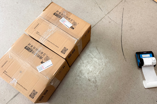 Brown cardboard shipping boxes staged next to a small label printer, illustrating the labeling and documentation requirements for lithium battery shipments under IATA DGR