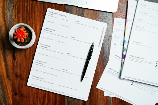 Documents and a ballpoint pen arranged on a wooden desk surface, representing the detailed written narrative required in a DOT special permit application to demonstrate equivalent level of safety